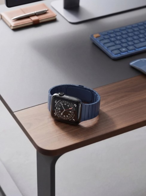 将图二的智能手表放到图一的木质桌面上，保证手表物理细节和桌子背景图内容绝对不变。手表是黑色金属表壳搭配深蓝色表带，表盘清晰，整体设计简约精致。精准匹配原场景透视角度，实现空间尺度物理融合，确保手表自然预览效果